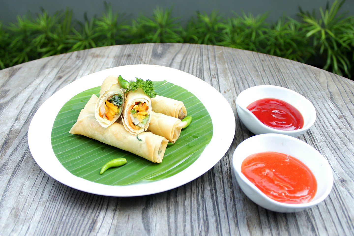 Golden-brown fried spring rolls on a banana leaf with dipping sauces.