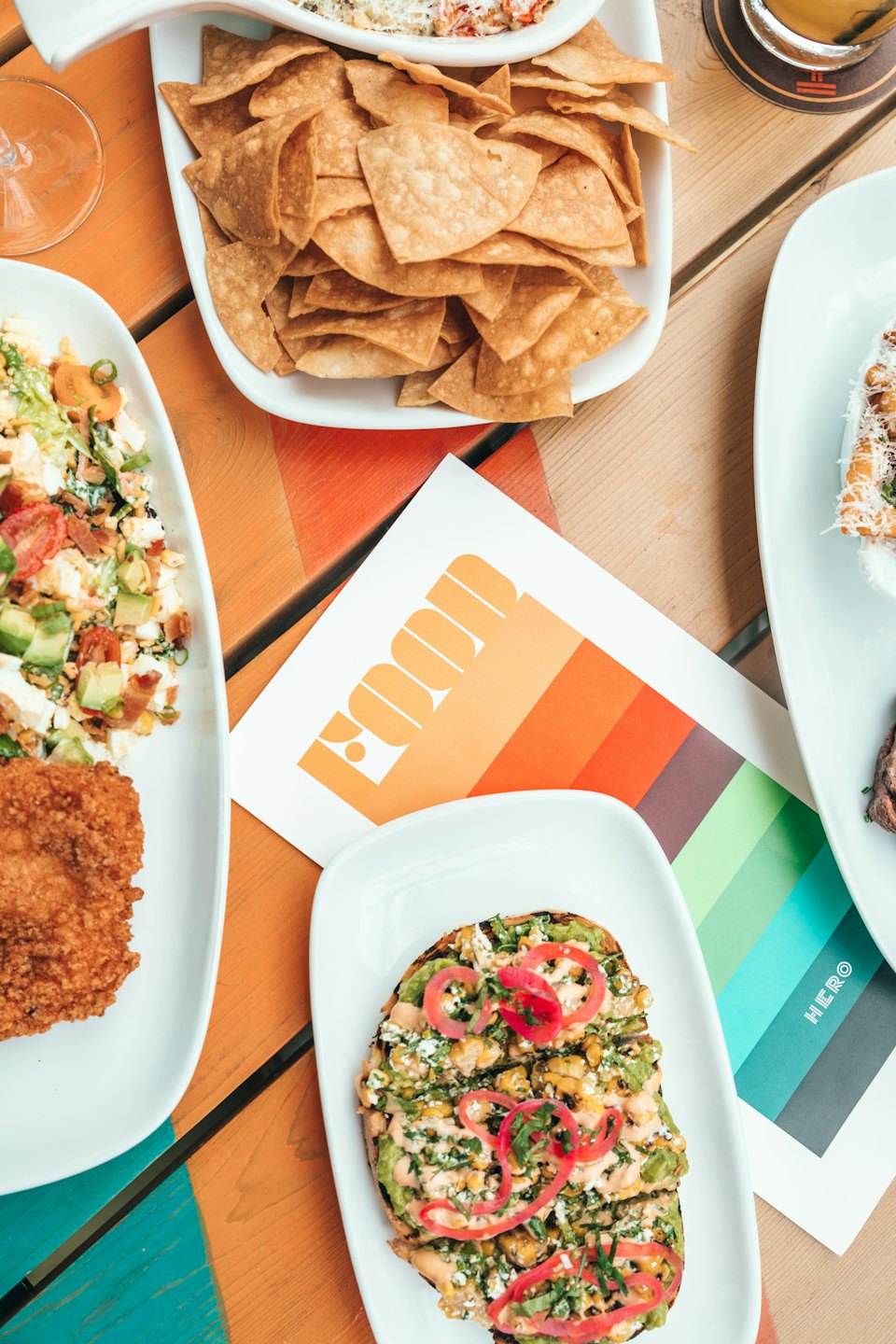 Colorful spread of tortilla chips, salad, and avocado toast on a wooden table.